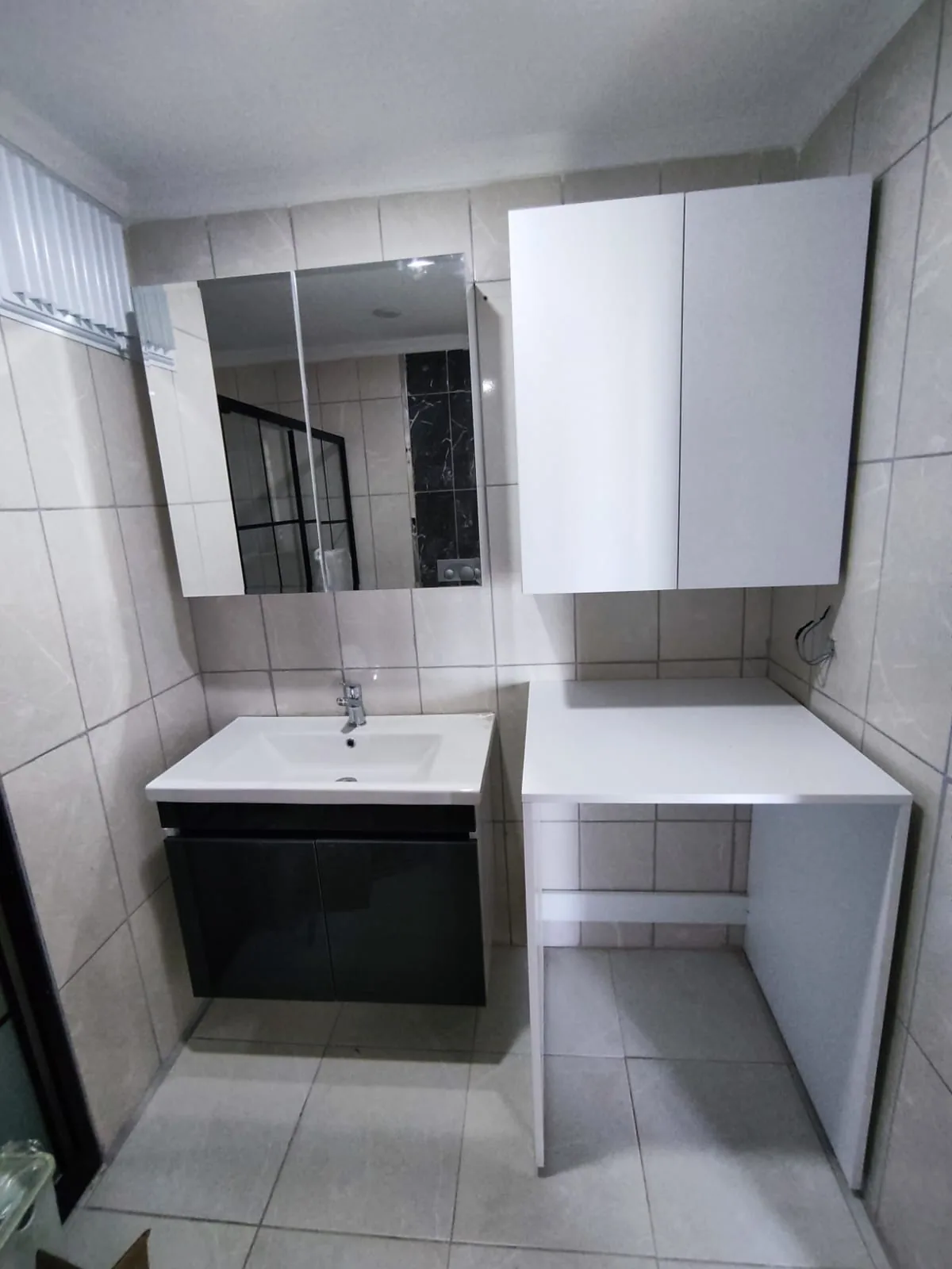 Çamaşır makinesi alanı, tezgâhı ve beyaz üst dolaplarıyla banyo depolaması