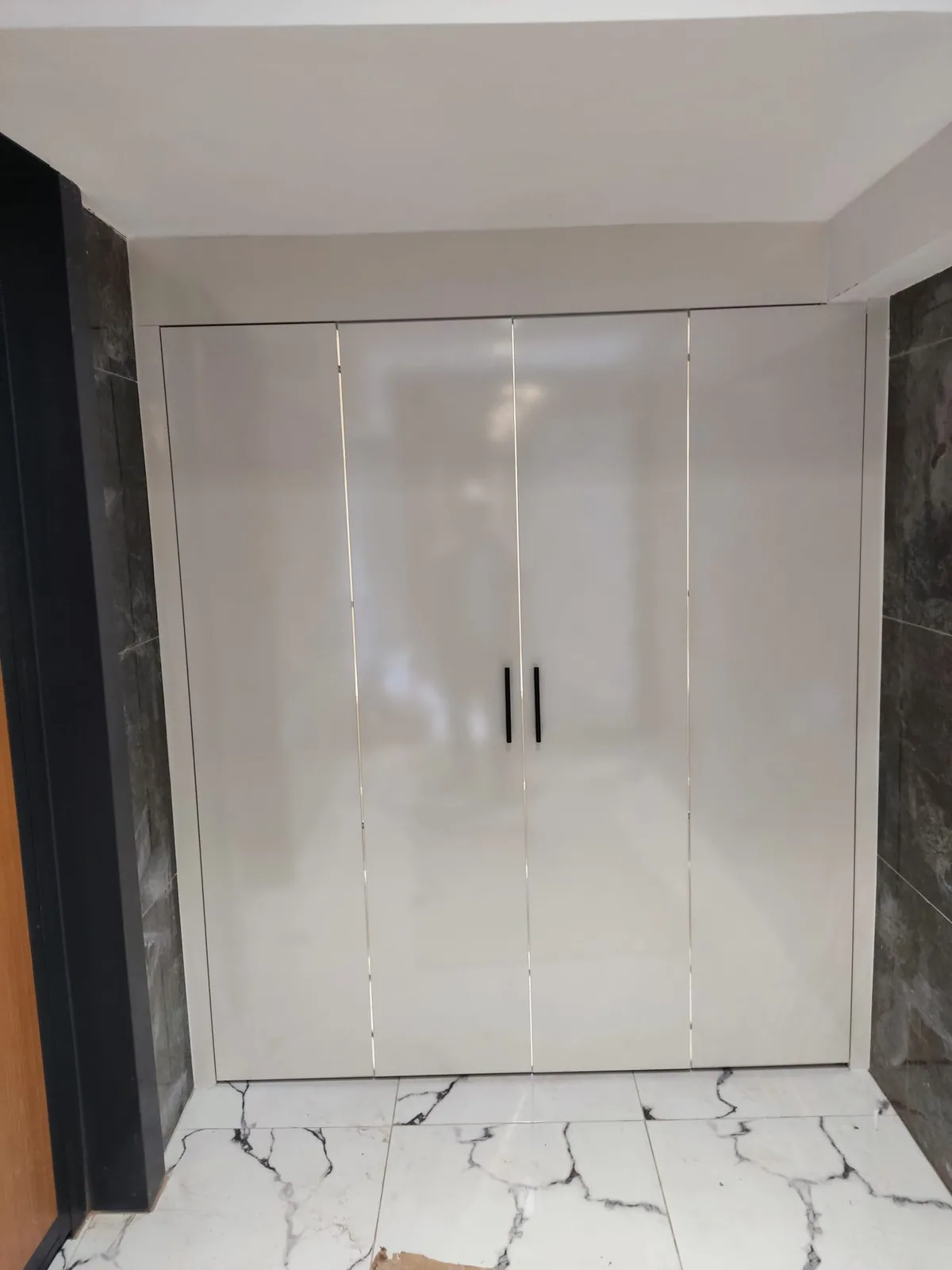 Duvar nişinde parlak beyaz kapaklı ve dikey kulplu gardırop